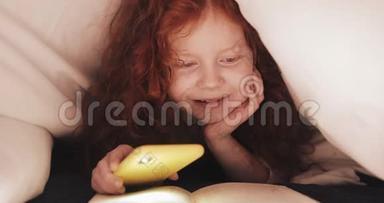 小红发女孩饶有兴趣地躺在他家的床上看书。女孩用智能手机的手电筒